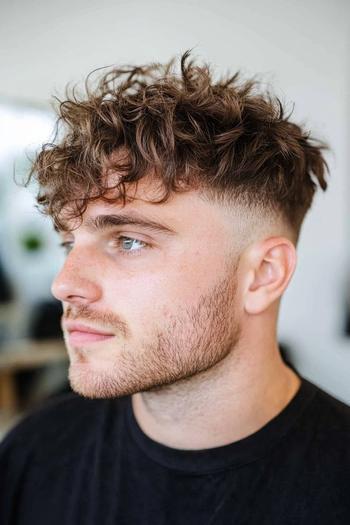 A man with a medium-length curly hairstyle featuring a faded undercut and a neatly groomed beard.