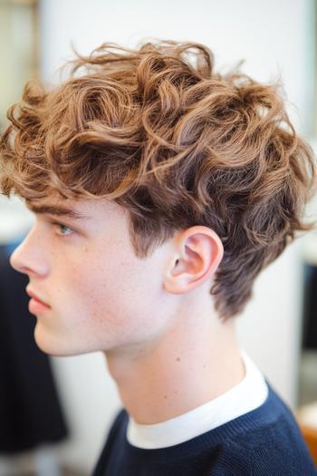 A young man with medium-length, wavy, and tousled hair, styled with volume and texture.