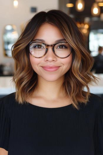 A woman with shoulder-length black hair styled in loose waves with brown highlights, wearing glasses and a black top.